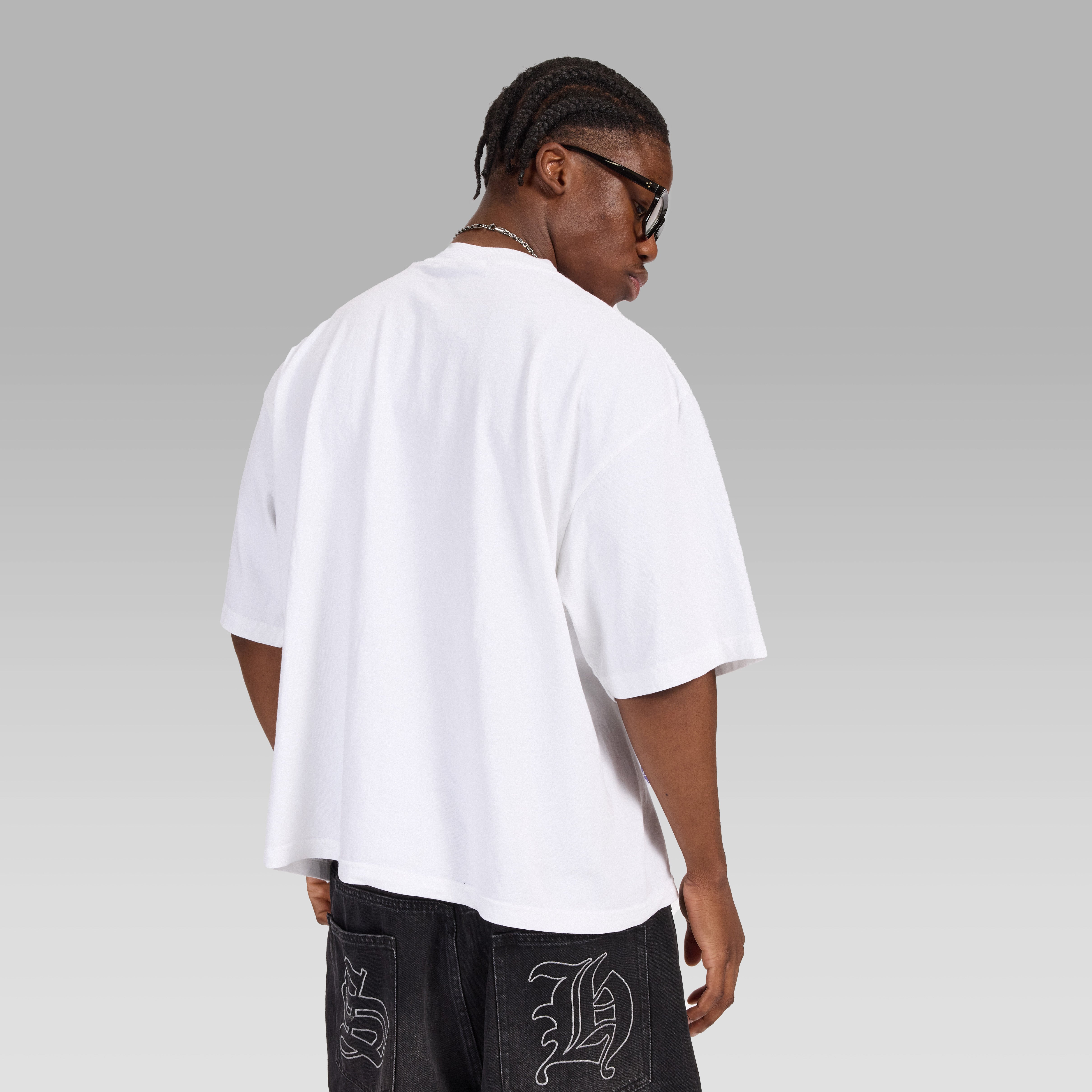 Person wearing a premium boxy streetwear style white t-shirt on a plain background showing the back only of the shirt