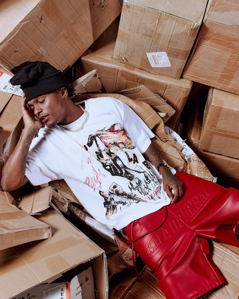 Person lying among cardboard boxes wearing a white t-shirt with graphic design and red shorts.